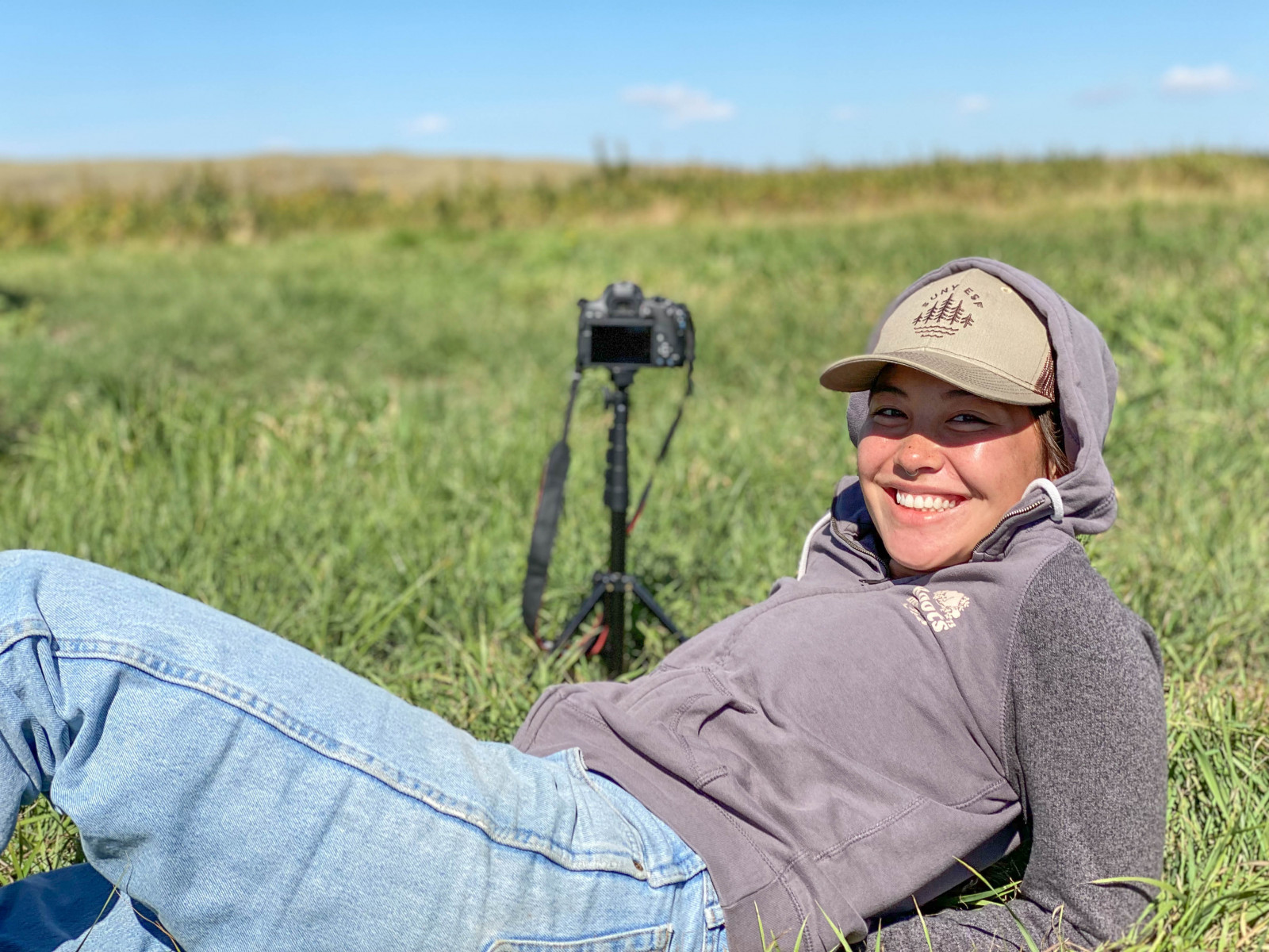 Eve relaxes in a field with her camera propped up behind her.